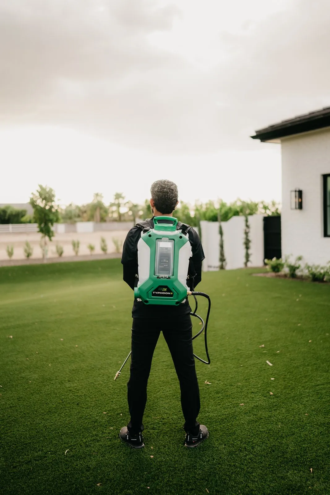 Citrus Pest Co technician carrying a backpack sprayer across a yard