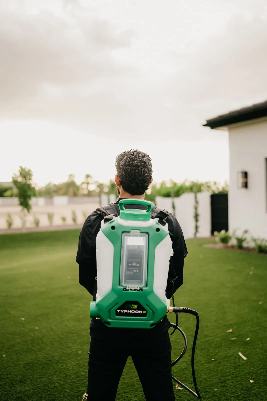 Citrus Pest Co technician carrying a backpack sprayer across a turf yard on a routine service visit