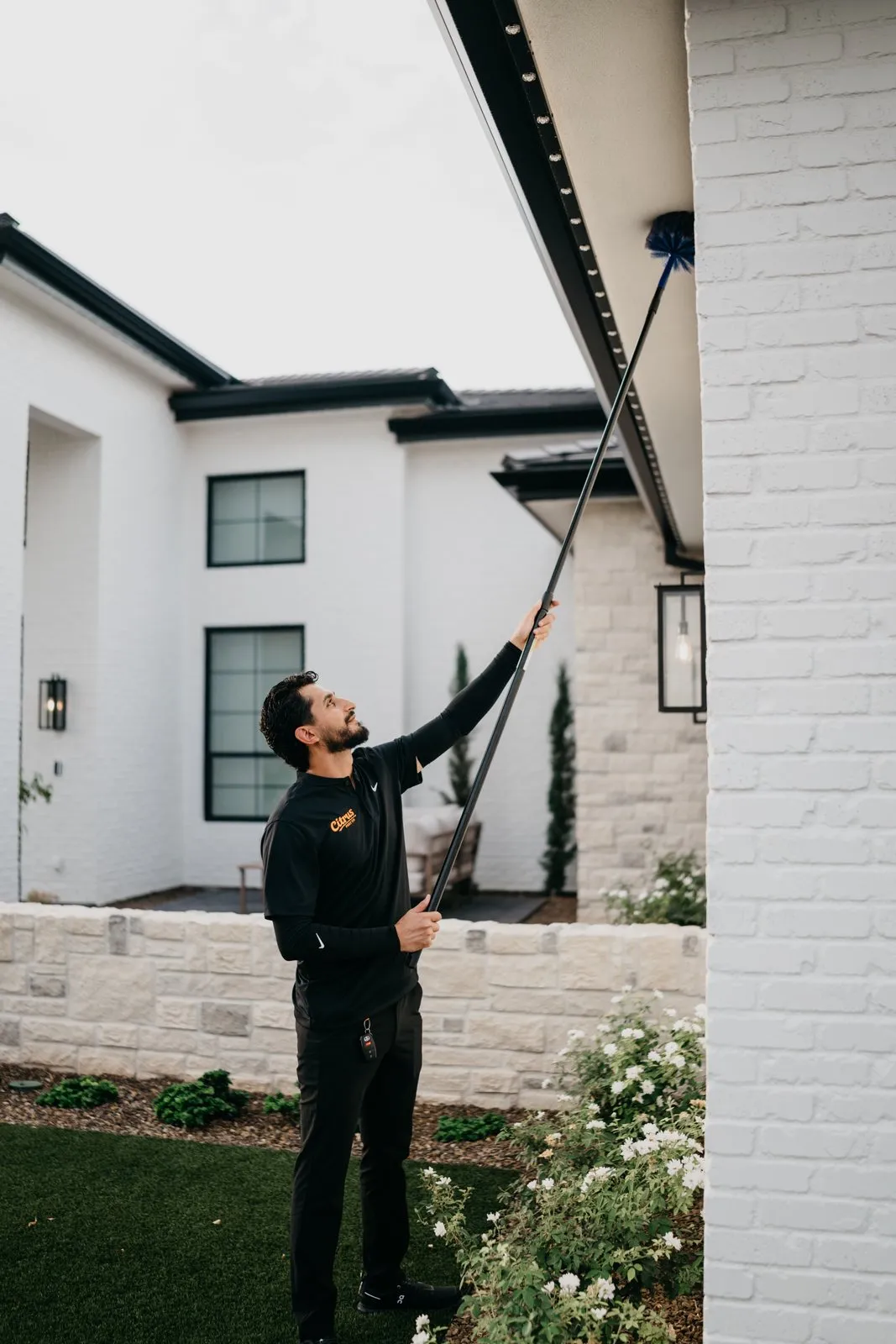 Citrus Pest Co technician clearing webs from a roofline with an extension pole