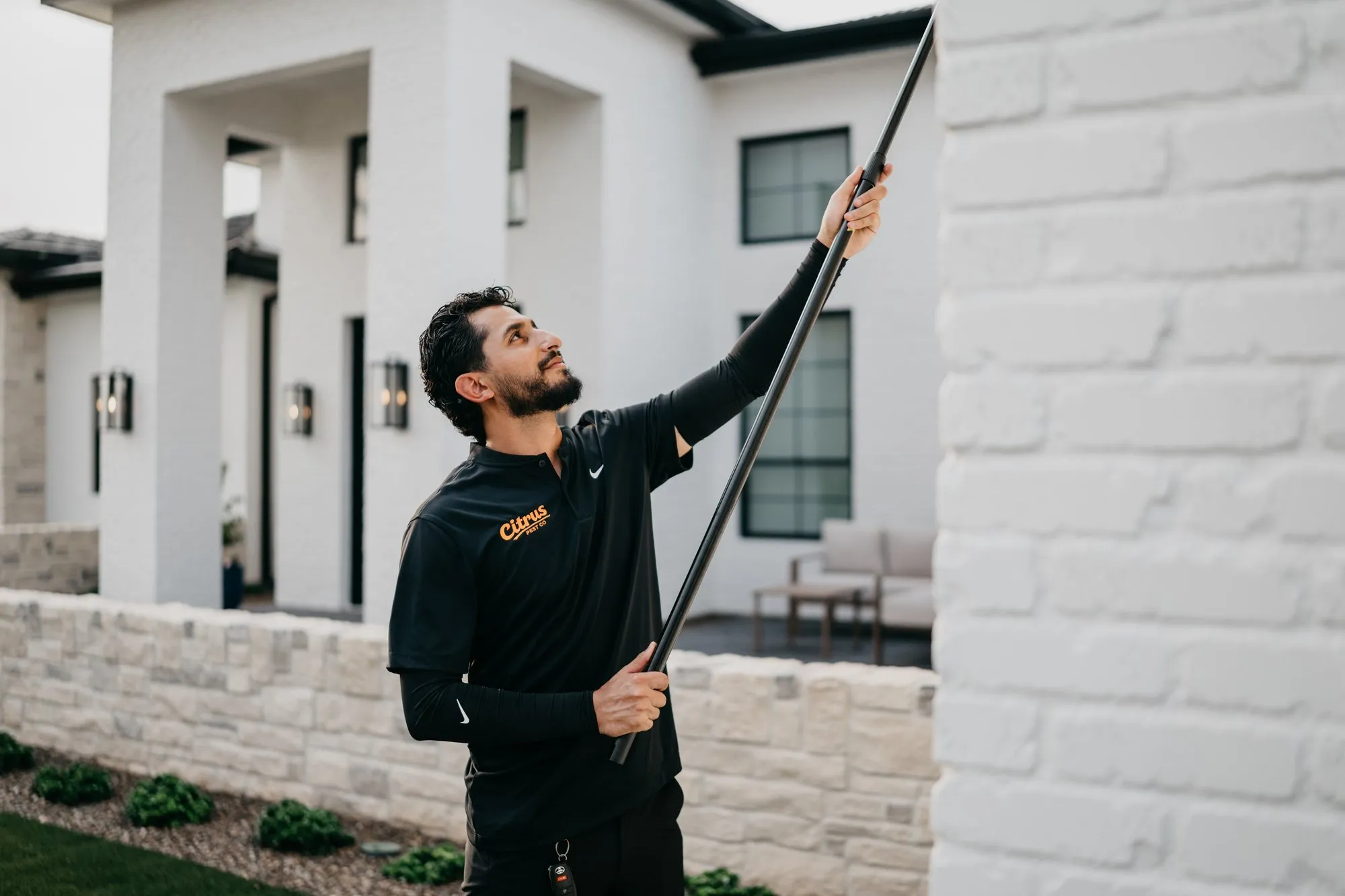 Citrus Pest Co technician using a long extension pole to clear webs from the eaves of a home