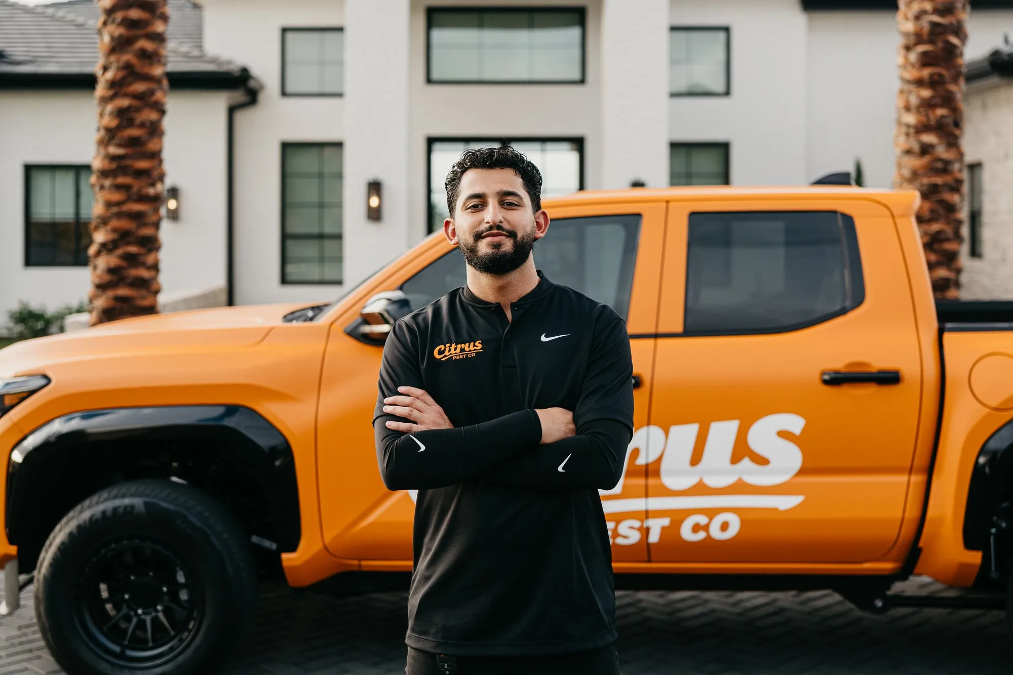 Citrus Pest Co owner standing with his arms crossed in front of the orange Citrus service truck outside an East Valley home
