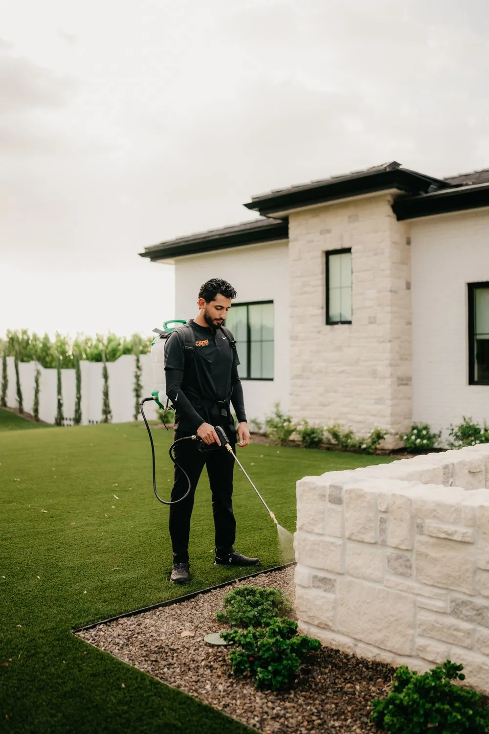 Citrus Pest Co technician treating a home exterior with a backpack sprayer
