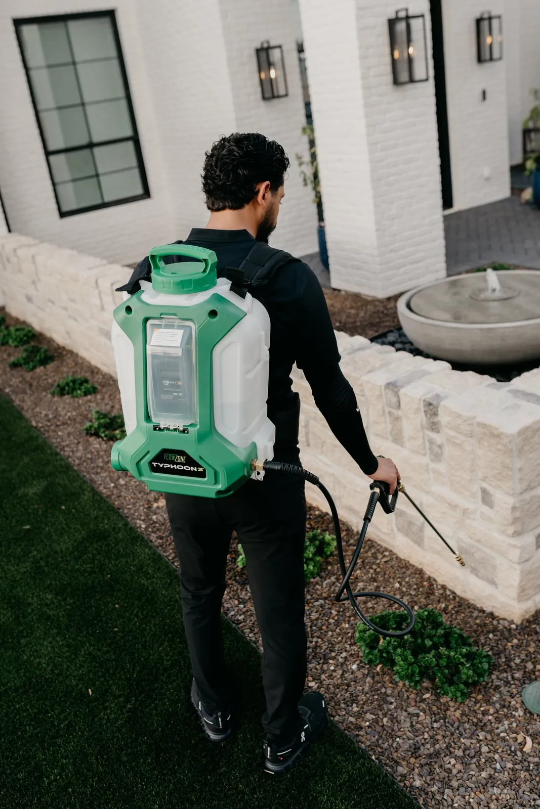 Citrus Pest Co technician treating a planting bed with a backpack sprayer, seen from behind