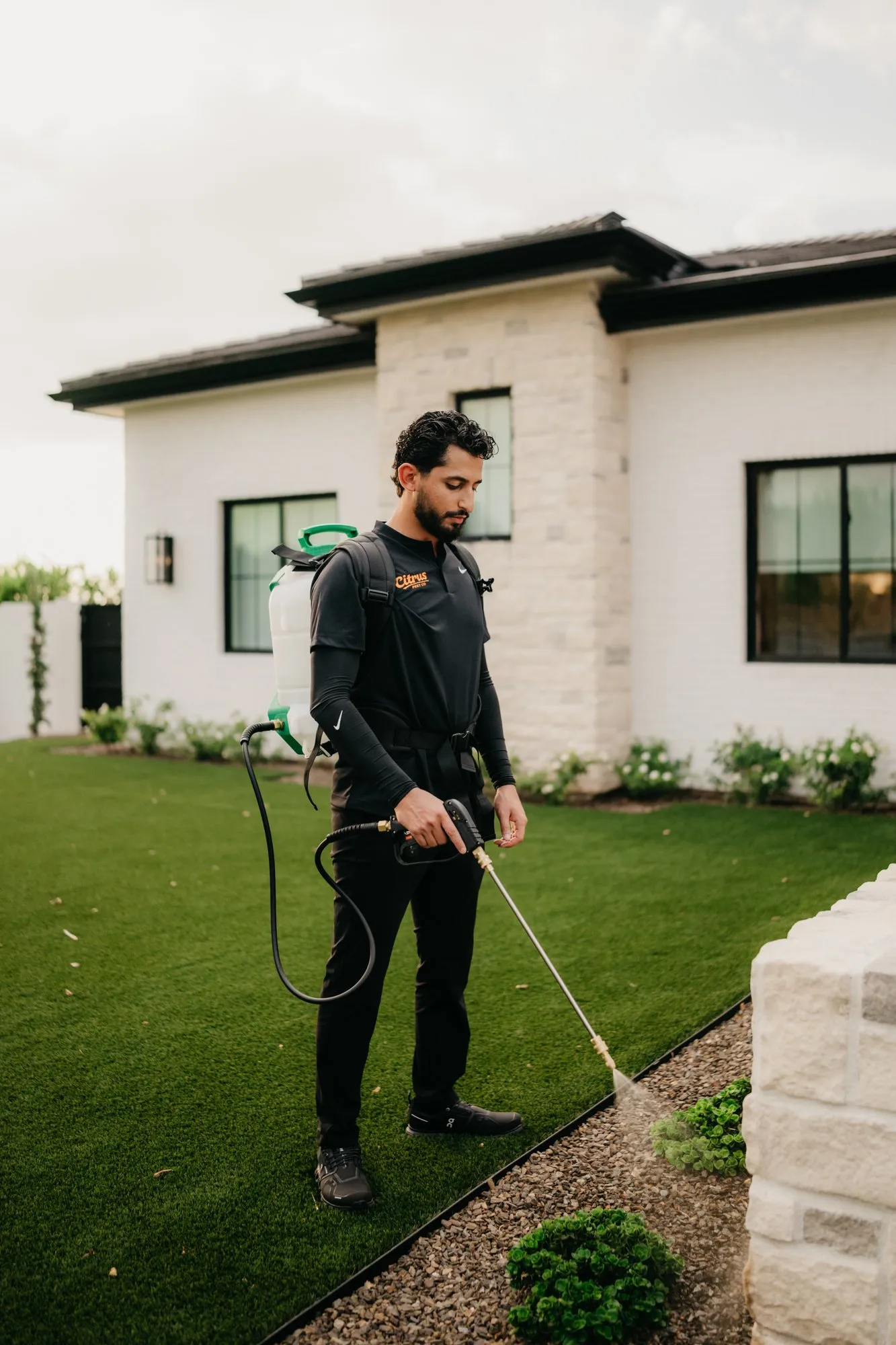 Technician spraying the foundation line and block wall perimeter of a desert home